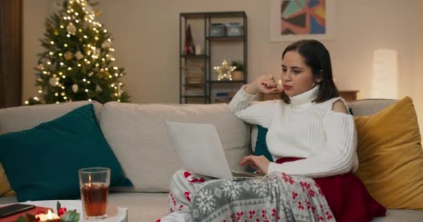 圣诞节那天 坐在圣诞树旁沙发客厅里的年轻女性在笔记本电脑上远程办公 她们上网 填写文件 与同事聊天 — 图库视频影像