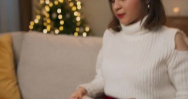 Dizüstü bilgisayarda çalışan genç bir kadın arka planda Noel ağacı olan bir koltukta oturuyor. Noel 'de uzaktan çalışma, işsizlik, yorgunluk....