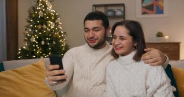 Noel dilekleri. İnternette sohbet eden mutlu genç bir çift akıllı telefondan ailelerine ve arkadaşlarına dilek diliyor. Noel arifesi uzaktan.