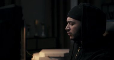 Hacker 'ın yeni görevi var. O, siyah giysiler giymiş, karanlık odada oturuyor. Arkada pizza kutuları var. Adam klavyeye yazı yazıyor ve kalemle not alıyor. Masada bir fincan kahve var..