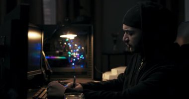 Siyah ceketli adam karanlık odadaki bilgisayar masasında oturuyor. Sakallı adam kalemi elinde tutuyor ve not alıyor. Önünde dosyaların yüklendiği monitörler var. Hacker bir görev üzerinde çalışıyor..