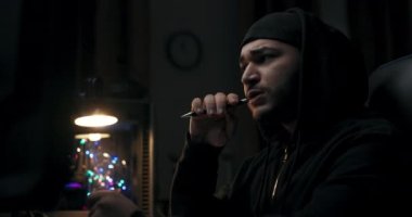 İşine odaklan, sakallı adam kalem tutuyor. Gergin bir şekilde kalemi bastırır ve kenara bırakır. Siyah şapkalı ve kazaklı adam bilgisayar klavyesinde yazmaya başlar. Önünde monitörler var..