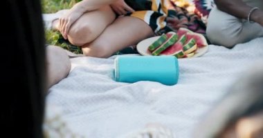 Hoparlörlerin çimlerin üzerinde piknik battaniyesine uzanmış hallerini yakından çek. Arkadaşlar dışarıda müzik dinleyerek ve eğlenerek vakit geçirirler..