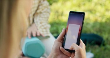 Kızın akıllı telefonuyla uygulamayı kullanarak hoparlörü eşleştirdiği telefonun yakın çekimi. Bluetooth 'u bağlamak ve açık havada müzik çalmak.