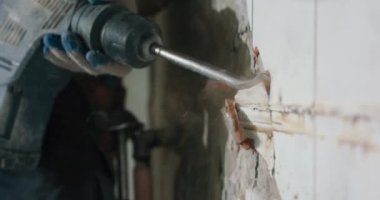 Daireyi yenileyen bir adamın yakın plan portresi. Güvenlik gözlüğü takan bir adam mutfak banyosunda çekiçle fayans çekiyor..