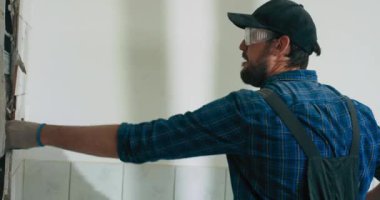 Odaklanmış adam tüm gücünü mutfak banyosunda fayansları çekiçlerken harcıyor. Tadilat sırasında inşaat alanında çalışan bir adam koruyucu eldivenlerle işini bitiriyor..