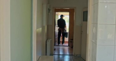 Gülümseyen memnun bir elektrikçi bir alet çantasıyla eve girer, lavaboyu tamir eder, daireyi yeniler. Gömlek, iş pantolonu ve şapka giymiş bir adam..