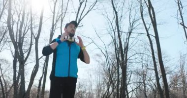 Sakallı, mavi ve siyah elbiseli bir adam koşmak için parka geldi. Keyfi yerinde, kulaklık takıyor, saati çalıştırıyor ve koşmaya başlıyor. Kafasında siyah bir şapka var..