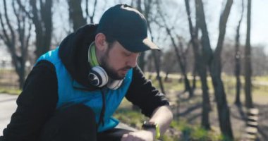 Parkta koşarken, sakallı genç adam çömeliyor ve ne kadar uzağa nöbet tuttuğuna bakıyor. O, siyah ve mavi giysiler giymiş ve başında bir şapkası var. Adam kalkar ve koşmaya devam eder.