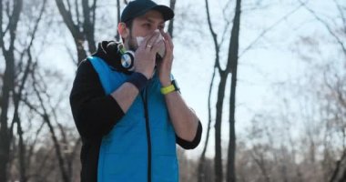 Adam parkta spor yapıyor. Güneşli bir kış sabahı, adam dondu ve sümüğü peçeteyle sildi. Siyah ve mavi elbiseler giyiyordu ve başında siyah bir şapka vardı. Adamın kulaklığı ve saati var.