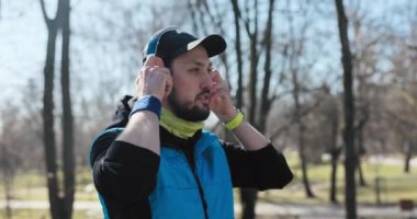 Sporcu sabah koşmak için parka geldi. O, siyah ve mavi giysiler giymiş ve şapkası var. Adam kulaklık takar, cebinden telefonu çıkarır, en sevdiği şarkıyı açar ve koşmaya başlar.