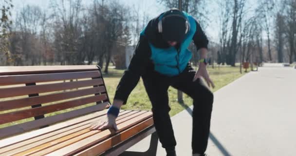 仕事の前の朝 若い男が公園で走っている 彼は休むためにベンチに座って 時計を見て 彼はまだ実行する必要がありますどのくらいかを確認します 男の子はフラストレーションにため息をつき 深呼吸をした — ストック動画