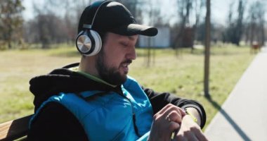 Sakallı adam bugün ne kadar uzağa koştuğunu görmek için bankta oturup saate bakıyor. O sonuçtan memnun, mutlu ve gülümsüyor. Adam kafasına siyah şapka ve kulaklık takmış. Derin nefes alıyor.