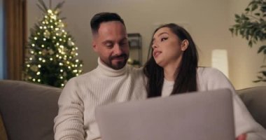 Uzun saçlı esmer kız ve sakallı adam kanepede oturuyor. Kız dizüstü bilgisayar tutuyor ve aşık çift Noel için hediye seçiyor. Gülümser ve kocasına ne sipariş etmesi gerektiği konusunda tavsiyelerde bulunur..
