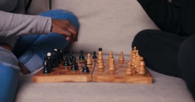 Satranç oynayan iki Afrikalı arkadaşın ellerinin yakın çekimi. Koltuğa oturup sırayla hamlelerini yapıyorlar. Çocuğun parmağında gümüş yüzük var. Çekici kız hareket eder ve gülümser.