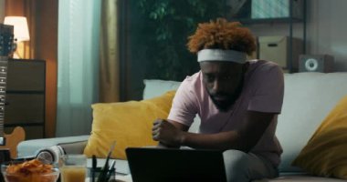 Afrika görünümlü genç adam iş toplantısına hazırlanıyor. Dizüstü bilgisayardaki sunumu izliyor ve dizüstü bilgisayardaki ana noktaları not alıyor. Masada bir kase cips ve meyve suyu var..