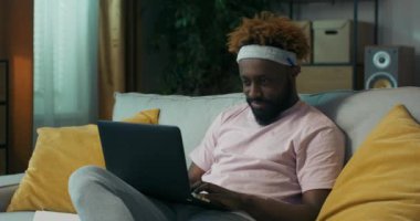 Sakallı, kıvırcık saçlı, Afrika görünümlü çekici bir adam dizüstü bilgisayarında web sitelerine göz atıyor ve deftere iş için yeni fikirler yazıyor. Kalemi kulağının arkasına koyar ve onunla yazar..