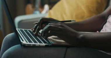 Kalem tutan ve dizüstü bilgisayar klavyesinde yazan Afrikalı bir çocuğun yakın çekimi. Sakallı ve kıvırcık saçlı adam iş arkadaşlarıyla görüntülü görüşme yapıyor. Saç bandı ve kulaklık takıyor..