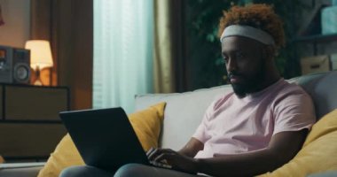 Kafasında bantla Afrika görünümlü genç bir adam, üzerinde sarı yastıklar bulunan kanepede oturuyor. Bir öğrenci dizüstü bilgisayarını kucağında tutuyor ve arkadaşlarıyla sohbet ediyor. Adam gülümsüyor..