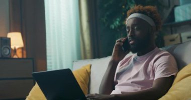 Afrikalı adam kanepede oturuyor, dizüstü bilgisayarını kucağında tutuyor ve makale yazıyor. Patron aradı ve makalenin yarın hazır olacağını söyledi. Adam hayal kırıklığına uğradı ve yazmaya devam etti..