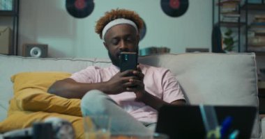 Afrika görünümlü çekici bir adam kanepede oturuyor. O, sarı yastıkların üzerinde dinlendi. Kafede tanıştığı bir kızdan telefon aldı. Gülümsedi ve telefonu açtı. Çocuk pembe tişört giyiyor..
