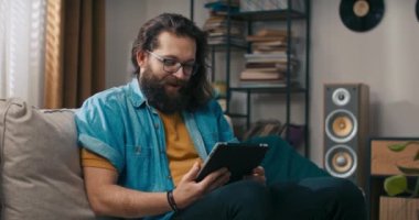 Mutlu bir adam elinde tabletle kanepede rahatlar, sosyal medyayı, internet sitelerini, online mağazaları gezer, bir uygulama aracılığıyla sipariş verir..