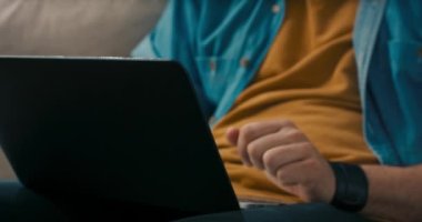 Dizüstü bilgisayardaki klavye tuşlarına basan bir el, kanepede dinlenen bir adam tarafından çekilmiş. Gözlüklü sakallı adam uzaktan çalışıyor, evrak dolduruyor, internete başvuruyor..