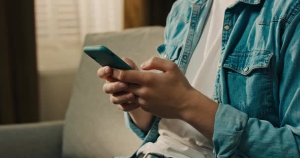 Ung Leende Man Jeansskjorta Sitter Soffa Vardagsrummet Studerande Håller Smartphone — Stockvideo