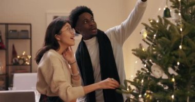 Arkadaşlar Noel 'i birlikte geçirecekler. Afro saçlı ve sakallı bir adam Kore kökenli gözlüklü bir kadınla konuşuyor. Noel ağacına bakıyor, takılara hayran..