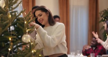 Süveter giyen kız ve kareli gömlekli Afrikalı çocuk Noel ağacının yanında duruyor. Süslemeleri ellerinde tutuyorlar ve asıyorlar. Birbirine aşık çiftler gülümser, kucaklaşır ve masaya geri döner..