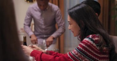 En iyi arkadaşlar doğum günü yemeği için toplandılar. Koyu renk uzun saçlı kız kaşıkları elinde tutuyor ve salatayı karıştırıyor. O, sıcak kırmızı kazak giyiyor. Arkadaşlar arkada yürüyor ve sohbet ediyorlar..