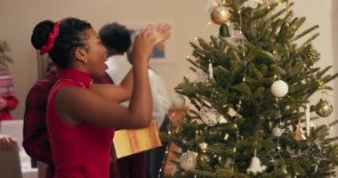 Noel partisi. Birbirine aşık bir çift Noel ağacının yanında duruyor ve süslemeler asıyor. Afrikalı görünümlü adamın elinde bir kutu süs var. Konuşuyorlar ve gülümsüyorlar. Öğrenciler eğleniyor..