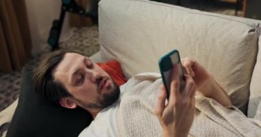 Bir adam oturma odasında kanepede uyuyor, öğle uykusundan uyanıyor telefonun çaldığını duyuyor ekrana bakıyor ve karısının kameraya el salladığını görüyor..