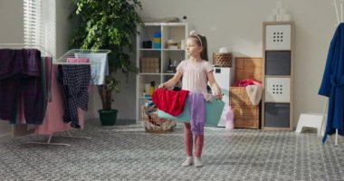 Küçük kız bir sepet çamaşır ile banyonun ortasında duruyor. Kız düşünceli bir şekilde uzağa bakıyor, gülümsüyor ve kameraya bakıyor. Banyoda çamaşır makinesi ve çamaşır asılıydı..