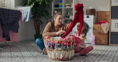 Beş yaşında bir kız ve teyzesi yerde oturup çamaşır yıkıyorlar. Kirli çamaşırları sepetten çıkarıp renklerine göre ayırıyorlar. İletişim kurup eğleniyorlar. Arkada çamaşır makinesi var..