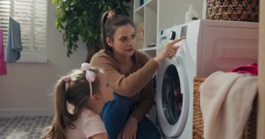 Güzel anne ve küçük kızı çamaşır yıkıyorlar. Kadın, kızına doğru çamaşır programını nasıl seçeceğini gösteriyor. Kız programı seçiyor, düğmeye basıyor ve ana şişeyi pembe pudrayla tutuyor..