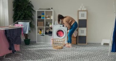 Genç kız çamaşır makinesinin yanında duruyor ve çamaşır yüklüyor. Programı seçti, oturdu, kollarını kavuşturdu, boş çamaşır sepetini aldı ve odadan ayrıldı. Yıkanmış giysiler banyoda asılı..