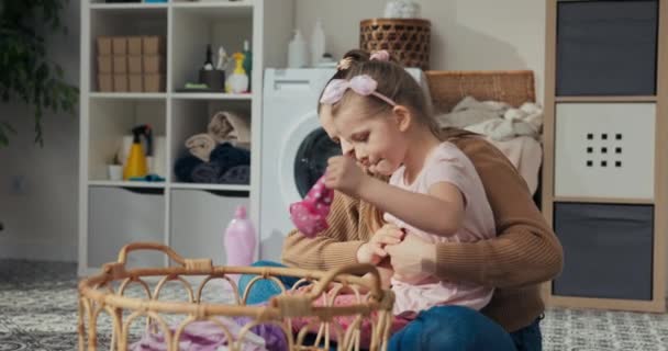 在浴室里 母亲和女儿坐在地板上 整理脏衣服洗 女孩从篮子里拿出衣服递给妈妈 女人拿出一双袜子 — 图库视频影像