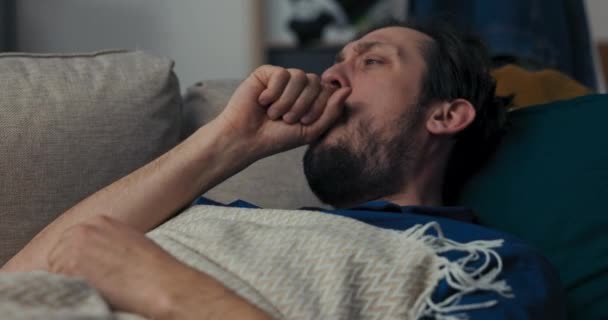 有胡子的病人躺在沙发上 睡在蓝色的枕头上 布鲁内特用毛毯盖住了自己 但咳嗽惊醒了自己 人开始大声咳嗽 睡着了 他感觉不舒服 — 图库视频影像