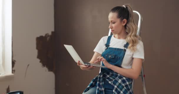 Dziewczyna Kręconymi Włosami Projektuje Mieszkanie Siedzi Drabinie Trzyma Laptopa Wybiera — Wideo stockowe