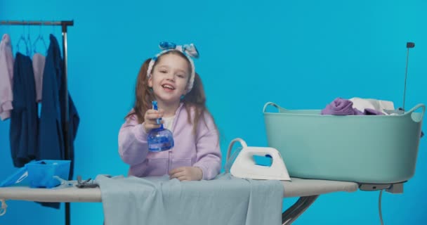 清洁女工是个能干的勤勤恳恳的姑娘 帮助做家务活 可爱的孩子站在蓝色工作室的背景上 手里拿着熨斗和铁罐 — 图库视频影像