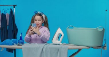 Küçük tatlı mutlu kız sosyal medyada vlog kaydediyor, arkadaşıyla sohbet ediyor, ev işi ütü yaparken kameraya el sallıyor..