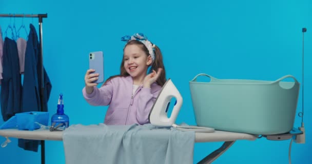 可爱可爱的小女孩在社交媒体上记录博客 与朋友聊天视频 一边做家务活一边烫衣服一边挥手拍照 — 图库视频影像