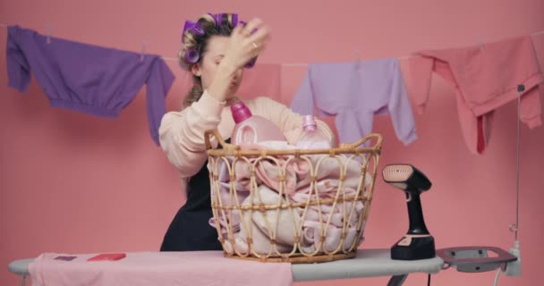 这个女人对做家务活很不满意 她用蒸汽船把柳条筐里的洗好的衣服拉了出来 粉红背景的家庭主妇画像 — 图库视频影像
