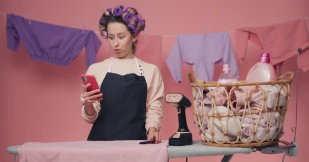 Woman Purple Curlers Standing Ironing Board Holding Phone Bank Card — Stock Video