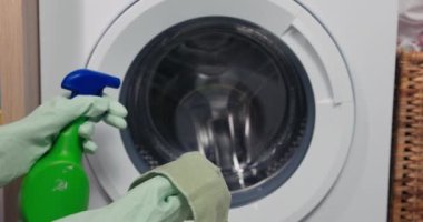 Sarı eldiven giymiş, çamaşır makinesinin içini bir bezle yıkayan bir kadının ellerinde..