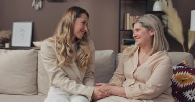 Anne ve kızı kanepede oturuyor, konuşuyor, el ele tutuşuyorlar. Kadın son sınıfa gününü ve işteki başarılarını anlatıyor. Mutluluk, neşe, destek.