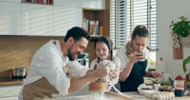 Önlüklü genç, tapılası anne lezzetli pizza malzemelerini masada hazırlarken, yakışıklı baban da anaokulu kızıyla birlikte un süzüyor..