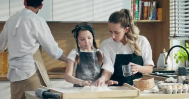 Önlüklü yakışıklı bir baba. Un ile el çırpıyor. Annem su dökerken yağ döküyor. Mutlu kız hamur yoğuruyor modern mutfakta ailelere yardım ediyor yerli pizza pişiriyor..