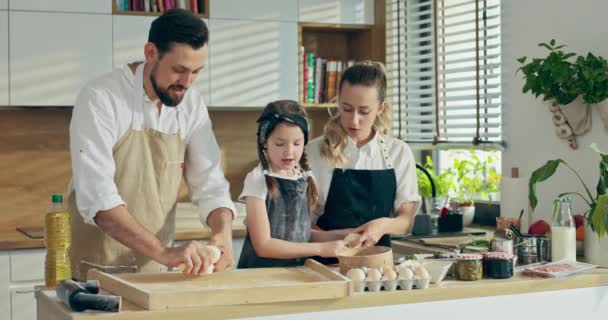 幸せな未就学児の娘で現代的なキッチンで若いお父さんとかなりお母さん混練生地で木製表面再生とともに調理ベーキングピザ — ストック動画